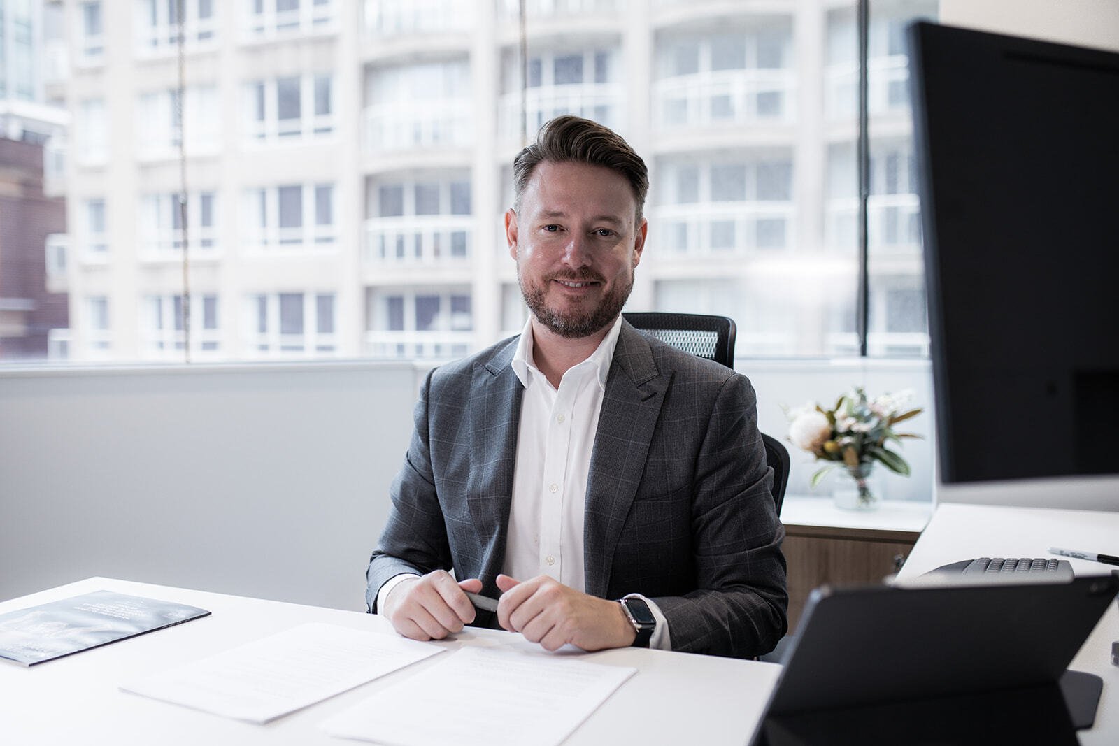 Chris sitting at office desk with papers on table and staring into camera smiling Chris sitting at office desk with papers on table and staring into camera smiling